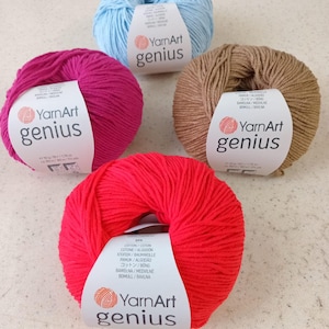 Pode incluir: Quatro novelos de fio YarnArt Genius em azul claro, magenta, bege e vermelho brilhante. Cada novelo possui uma etiqueta de papel branco com o nome da marca e detalhes do produto, incluindo um peso de 50 gramas e 160 metros por novelo.