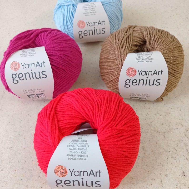 Pode incluir: Quatro novelos de fio YarnArt Genius em azul claro, magenta, bege e vermelho brilhante. Cada novelo possui uma etiqueta de papel branco com o nome da marca e detalhes do produto, incluindo um peso de 50 gramas e 160 metros por novelo.