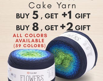 Pode incluir: Dois novelos de fio YarnArt Flowers com um gradiente de cor que transita do azul marinho escuro para o azul brilhante e verde lima. As etiquetas de papel branco exibem a marca, o nome do produto e instruções de cuidado em preto.