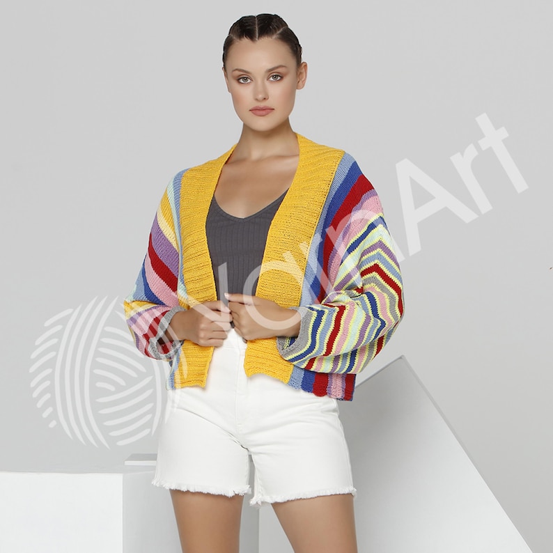 Pode incluir: Um cardig&atilde; de malha curto com um padr&atilde;o vibrante de riscas multicoloridas em tons de amarelo, vermelho, azul e branco. A pe&ccedil;a apresenta uma borda frontal canelada em amarelo s&oacute;lido, mangas compridas com punhos canelados e design aberto.