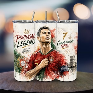 May include: A cylindrical tumbler with a metal straw featuring a watercolor-style portrait of a soccer player in a red and green jersey. Text includes Portugal Legend, Born for Greatness, 7 Championship Spirit, and a signature on a white background.