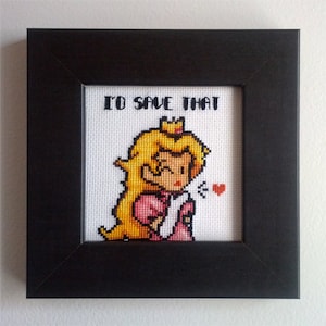 May include: Cross-stitch artwork in a black frame featuring Princess Peach from the Super Mario video game series. The artwork includes the text "I'D SAVE THAT" above the character, with a small red heart.