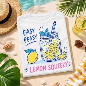 Puede incluir: Camiseta blanca con un diseño colorido con temática de limón. El diseño incluye un tarro con limonada, rodajas de limón y el texto "Easy Peasy Lemon Squeezy". También se ven un sombrero de paja, gafas de sol y un vaso de limonada.