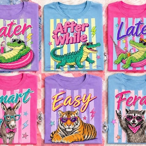Puede incluir: Una colección de camisetas coloridas con gráficos de animales de dibujos animados. Cada camiseta presenta un animal diferente, como un caimán, un burro, un tigre y un mapache, con gafas de sol. Las camisetas tienen textos como "Later", "After While", "Smart", "Easy" y "Feral".