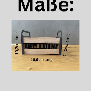 May include: A wooden box with the words "HAPPY BIRTHDAY" cut out. The box is 16.6 cm long, 10.2 cm high, and 11.1 cm wide. It has black handles on each end.