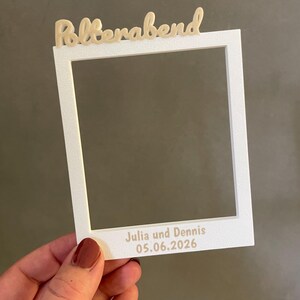 Könnte beinhalten: Ein weißer rechteckiger Fotorahmen mit strukturierter Oberfläche. Am oberen Rand steht das Wort Polterabend in einer hellbeigen Schreibschrift. Am unteren Rand befinden sich der Text Julia und Dennis sowie das Datum 05.06.2026 in serifenloser Schrift.