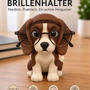 Könnte beinhalten: Eine braun-weiße Beagle-Hunde-Figur als Brillenhalter mit großen dunklen Augen, die eine Brille mit Schildpattmuster trägt. Darüber steht der Text BEAGLE BRILLENHALTER, ergänzt durch weiteren deutschen Text unterhalb der Hundefigur.