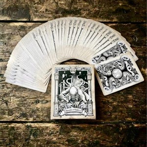 May include: A deck of playing cards fanned out with a box featuring a black and white illustration of a creature and the text 'Legends of Cthulhu'. The card backs display a detailed black and white pattern of tentacles and a central circular emblem.