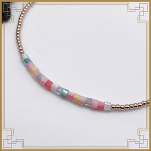 May include: A delicate bracelet with a strand of small, rose gold beads and a section of colourful, square-shaped beads. The square beads are in pastel shades of pink, yellow, green, and grey. The bracelet is on a white background.