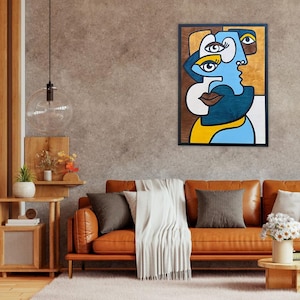 Puede incluir: Obra de arte abstracto que representa un rostro estilizado en azul, marrón y amarillo. La obra está enmarcada en negro y cuelga de una pared texturizada. El diseño incluye múltiples ojos y una boca prominente.