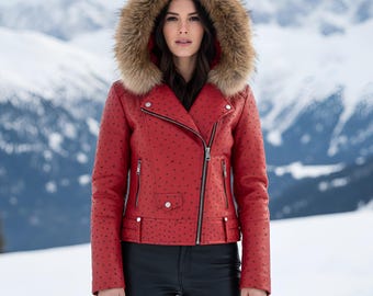 Könnte beinhalten: Rote Lederjacke mit fellbesetzter Kapuze. Die Jacke hat einen diagonalen Reißverschluss, mehrere Taschen und ein gepunktetes Muster. Das Model trägt eine schwarze Hose, mit schneebedeckten Bergen im Hintergrund.