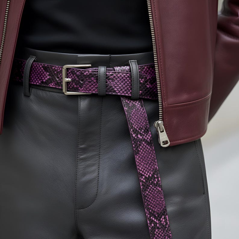 May include: A close-up of a purple snakeskin belt with a silver buckle, worn with black leather pants and a burgundy leather jacket. The belt's pattern is a mix of purple and black, adding a bold accent to the outfit.