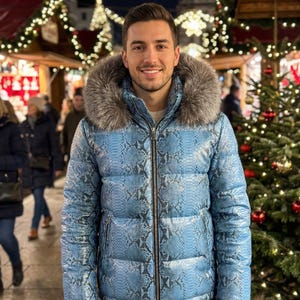 May include: A light blue puffer jacket with a snakeskin pattern and a fur-lined hood. The jacket has a zip closure. The person is wearing the jacket outdoors, with Christmas decorations in the background.