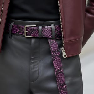 May include: A close-up of a purple snakeskin belt with a silver buckle, worn with black leather pants and a burgundy leather jacket. The belt is the focal point, showcasing its unique pattern and color.