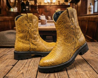 May include: A pair of yellow cowboy boots with a snakeskin pattern. The boots have a black sole and a short heel. The boots are made of a textured material and are sitting on a wooden surface.