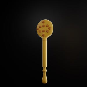 Puede incluir: Una cuchara de cocina amarilla con una cabeza redonda con acentos circulares marrones. El mango es largo y delgado, con una base decorativa y redondeada. La cuchara está sobre un fondo negro.