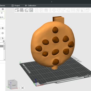 Puede incluir: Modelo 3D de una galleta marr&oacute;n claro con varios agujeros. El modelo se muestra sobre una cuadr&iacute;cula gris, con una interfaz de impresora 3D visible en el fondo.
