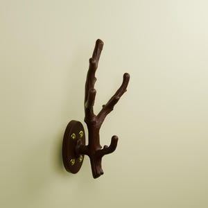 May include: A dark brown wall-mounted hook shaped like a tree branch with multiple prongs for hanging items. The hook features a circular base plate secured to the wall with four visible gold-colored screws, providing a sturdy mounting point.