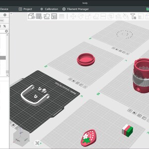May include: A 3D printing software interface displaying a digital workspace with multiple build plates. The screen shows various 3D models including a cylindrical container with a strawberry motif, a handle, and a small strawberry-shaped emblem.