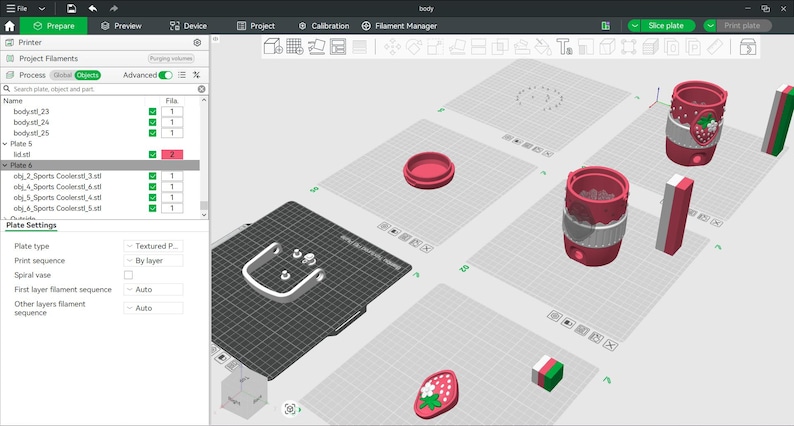 May include: A 3D printing software interface displaying a digital workspace with multiple build plates. The screen shows various 3D models including a cylindrical container with a strawberry motif, a handle, and a small strawberry-shaped emblem.