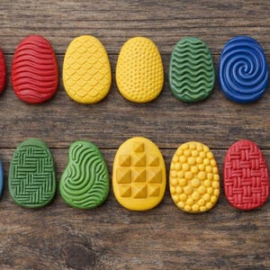 May include: A collection of twelve colorful, textured Easter egg decorations in red, yellow, green, and blue. Each egg has a unique pattern, including lines, swirls, and geometric shapes. The eggs are arranged on a rustic wooden surface.