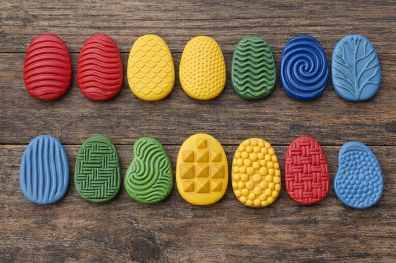 May include: A collection of twelve colorful, textured Easter egg decorations in red, yellow, green, and blue. Each egg has a unique pattern, including lines, swirls, and geometric shapes. The eggs are arranged on a rustic wooden surface.