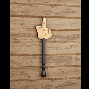 Pode incluir: Um tampão de garrafa com design de dedo do meio em madeira e cabo preto. A mão é feita de madeira clara, com uma representação detalhada dos dedos e da unha. O cabo preto adiciona um toque de humor ao acessório de bar.
