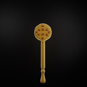 Puede incluir: Utensilio de cocina amarillo con una cabeza redonda y un mango largo. La cabeza presenta varios acentos marrones y circulares. El mango tiene un dise&ntilde;o decorativo en la parte inferior. El fondo es negro s&oacute;lido.