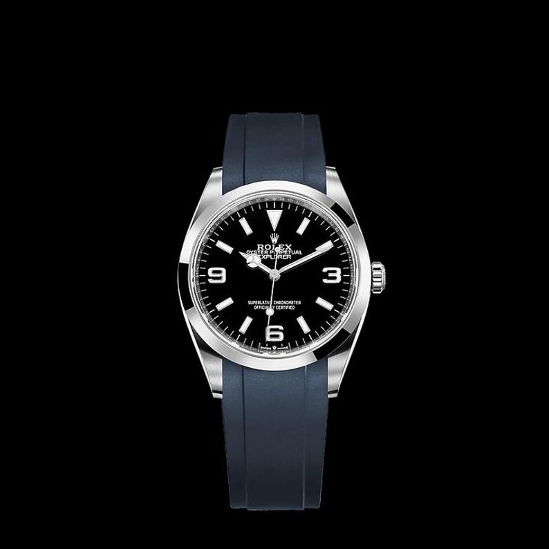 K&ouml;nnte beinhalten: Eine Luxus-Armbanduhr mit schwarzem Zifferblatt, silberfarbenem Geh&auml;use und dunkelblauem Kautschukarmband. Das Zifferblatt hat wei&szlig;e Stundenmarkierungen und Zeiger, mit Markennamen und Modelldetails. Die Uhr ist vor schwarzem Hintergrund.