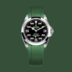 May include: A Rolex Air King watch with a black dial, silver bezel, and green rubber strap. The watch face displays white numerals and hands against a black background. The watch is set against a dark green backdrop.