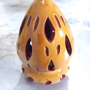 May include: A ceramic candle holder with a yellow-orange glaze and oval cutouts. The base is a lighter yellow with dark red polka dots. The candle holder has a cracked, aged appearance. The height is approximately 10 cm.