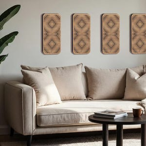 May include: Four rectangular wooden wall panels with a geometric dot pattern are mounted on a light gray wall. Below, a beige sofa with several pillows sits in front of a small, round, dark brown coffee table.