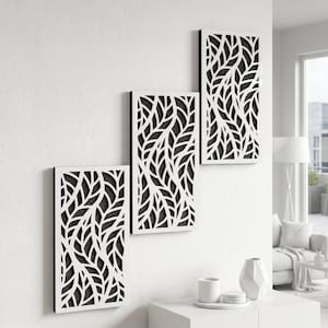 Puede incluir: Tres paneles de arte mural rectangulares con un diseño de hojas. Los paneles son blancos con un fondo negro, creando un aspecto de alto contraste. El patrón de hojas es intrincado y detallado, agregando un toque de naturaleza a la decoración.