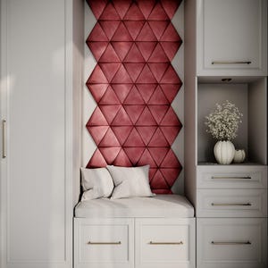 Puede incluir: Un mueble empotrado blanco con un banco acolchado y cajones. La pared trasera presenta un patrón geométrico de paneles triangulares rojos. Dos almohadas blancas descansan sobre el banco. Un jarrón con flores blancas se encuentra en un nicho.