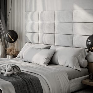 May include: A modern bedroom with a large bed featuring a gray headboard and bedding. Two spherical black pendant lights hang above the bed. A gray and white cat is curled up on the bed. The room has a neutral color palette.