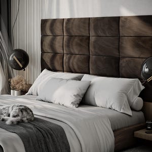 May include: A modern bedroom with a large bed featuring a dark brown, square-paneled headboard. The bed is made with white bedding and gray accents. Two black globe pendant lights hang above the bed. A cat is sleeping on the bed.