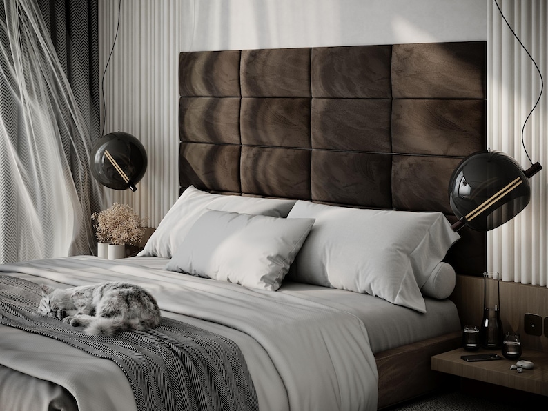 May include: A modern bedroom with a large bed featuring a dark brown, square-paneled headboard. The bed is made with white bedding and gray accents. Two black globe pendant lights hang above the bed. A cat is sleeping on the bed.