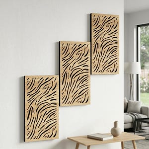 Op de afbeelding: Set van drie rechthoekige wandkunstpanelen. Elk paneel heeft een natuurlijke houtnerf achtergrond met een zwart, zebra-achtig patroon. De panelen zijn gemonteerd op een witte muur, waardoor een modern, abstract ontwerp ontstaat.