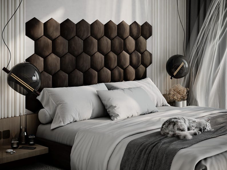 Puede incluir: Un dormitorio moderno con un cabecero marr&oacute;n oscuro con dise&ntilde;o de panal. La cama est&aacute; hecha con ropa de cama blanca y gris claro, y una manta gris. Dos l&aacute;mparas colgantes negras en forma de globo cuelgan sobre la cama. Un gato est&aacute; durmiendo en la cama.