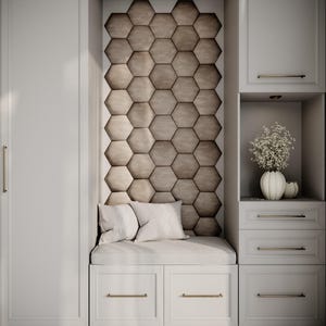 Puede incluir: Un mueble empotrado blanco con zona de estar. La pared trasera presenta un diseño de panal de abeja. La zona de estar tiene cojines y almohadas blancos. Un jarrón con flores se encuentra en una estantería. Los tiradores dorados adornan los cajones y las puertas.