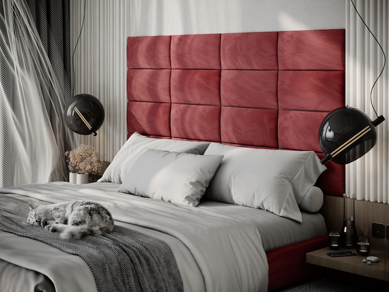May include: A modern bedroom with a red upholstered headboard, gray bedding, and decorative black globe pendant lights. A gray and white cat is curled up on the bed. The room has a minimalist design.