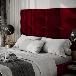 May include: A luxurious bedroom scene featuring a bed with a deep red, tufted headboard. The bed is made with white bedding and gray accents. A gray and white cat is curled up on the bed. Modern black globe pendant lights hang above.