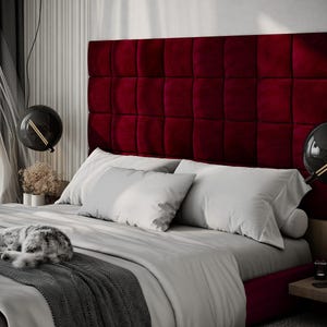 May include: A luxurious bedroom scene featuring a bed with a deep red, tufted headboard. The bed is made with white pillows and a gray comforter. A sleeping cat rests on the bed. Modern black globe pendant lights hang above the bed.