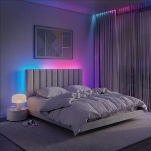 May include: A light grey upholstered bed with a vertical channel-tufted headboard, dressed in matching grey bedding. A mushroom-shaped table lamp sits on a cylindrical nightstand, with vibrant blue and pink LED accent lighting on the wall.