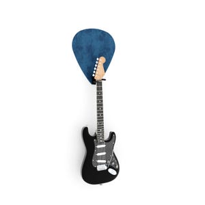 May include: A black electric guitar with a white pickguard and a wooden neck is mounted on a wall. A large, blue, guitar pick-shaped wall mount is behind the guitar's headstock, creating a unique display.