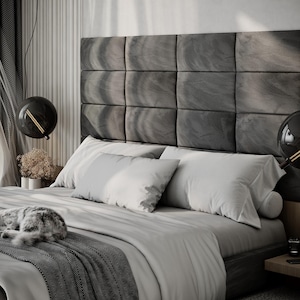 May include: A modern bedroom with a large bed featuring a gray headboard composed of square panels. The bed is covered with white and gray bedding, and a gray cat is curled up on the bed. Two black globe pendant lights hang above the bed.