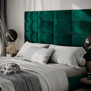 May include: A luxurious bedroom scene featuring a bed with a large, emerald green, tufted headboard. The bed is made with white pillows and a gray comforter. A sleeping cat rests on the bed. Modern black globe pendant lights hang above the bed.