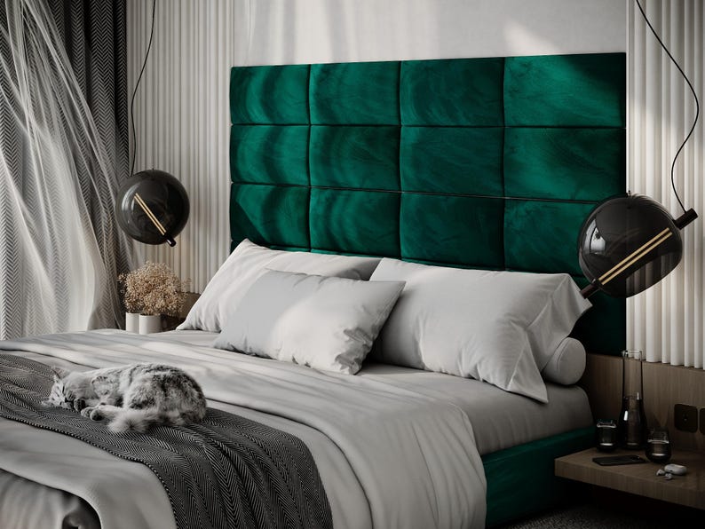 May include: A luxurious bedroom scene featuring a bed with a large, emerald green, tufted headboard. The bed is made with white pillows and a gray comforter. A sleeping cat rests on the bed. Modern black globe pendant lights hang above the bed.
