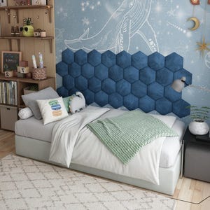 May include: A modern bedroom setup featuring a bed with a white comforter and a green knitted throw blanket. A blue hexagon-shaped wall panel serves as a headboard. Decorative pillows and a rug complete the cozy space.