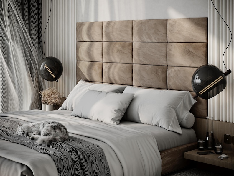 May include: A modern bedroom with a large bed featuring a tufted headboard and gray bedding. Two black globe pendant lights hang above the bed. A gray and white cat is curled up on the bed.